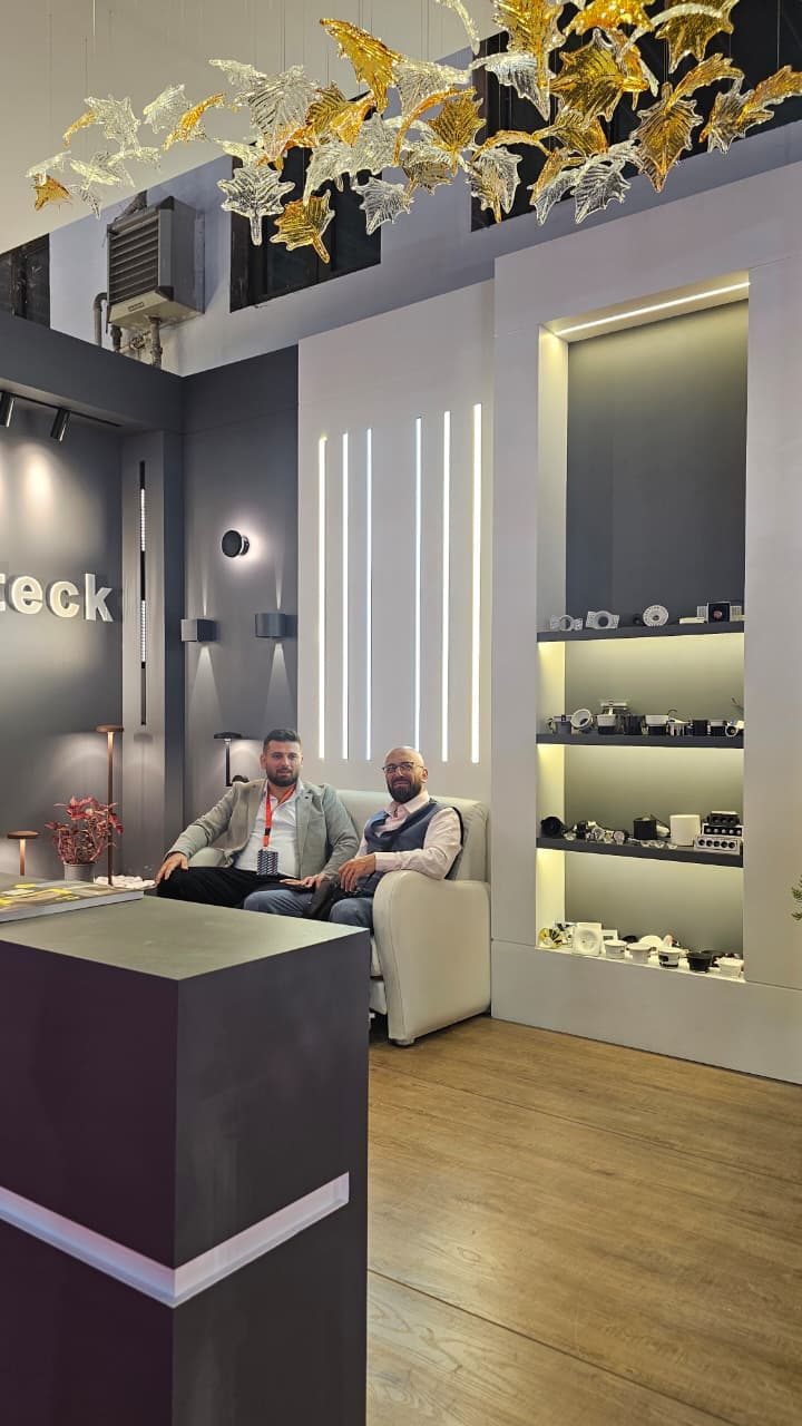 The seating corner of the stand, with a lit display niche of spotlights and accessories and two colleagues in conversation.
