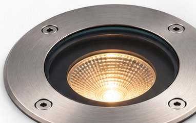 An in-ground uplight set flush into paving, washing the wall above it.